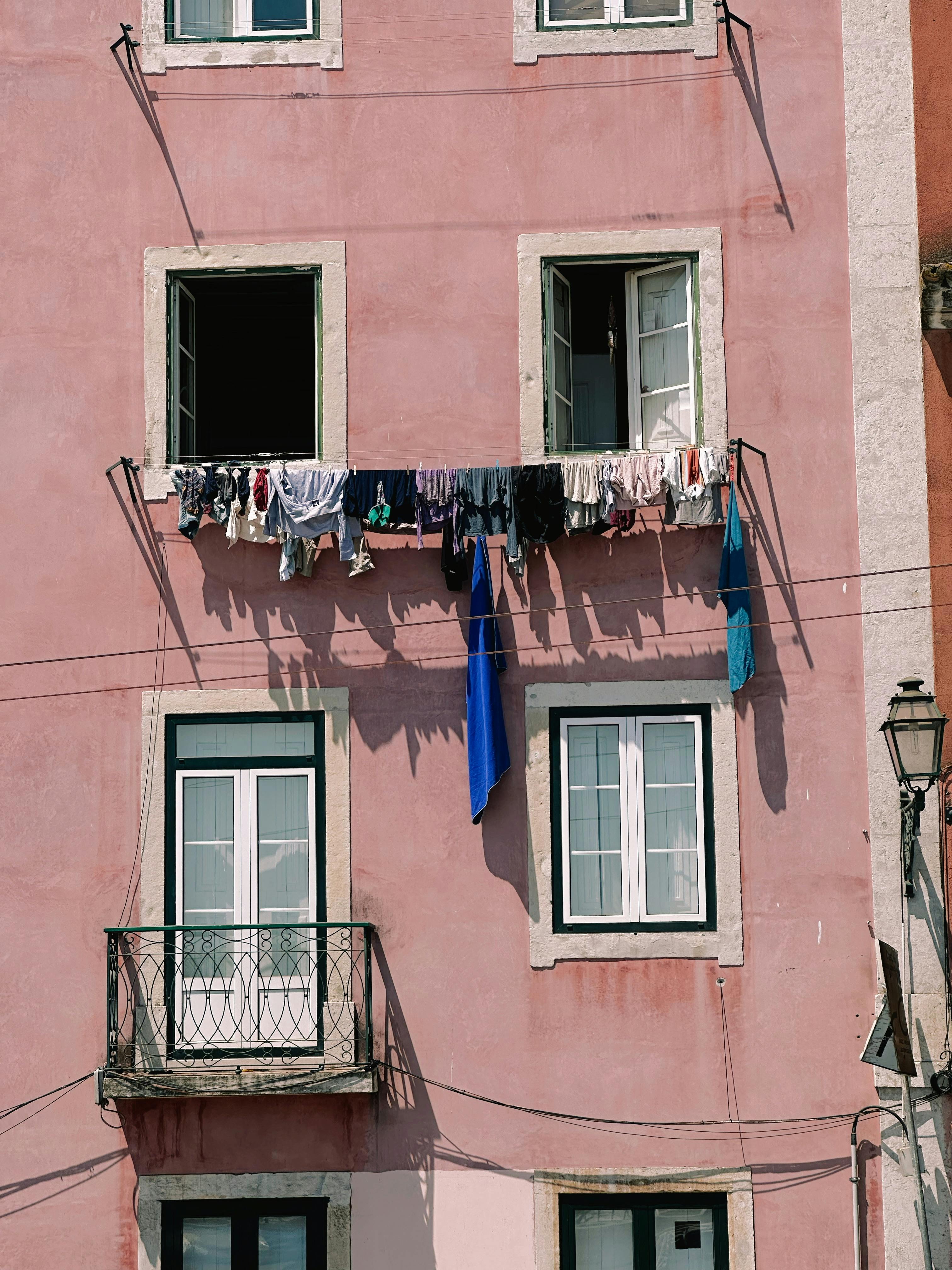 Vibrant clothes drying on a pink building facade under clear daylight.