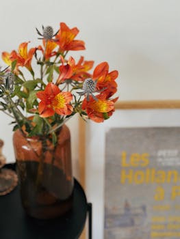 Orange flowers in a vase on a table, with a blurred poster in the background.
