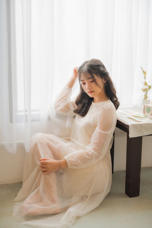 Free Young woman in white dress by window, exuding calm elegance and serenity indoors. Stock Photo