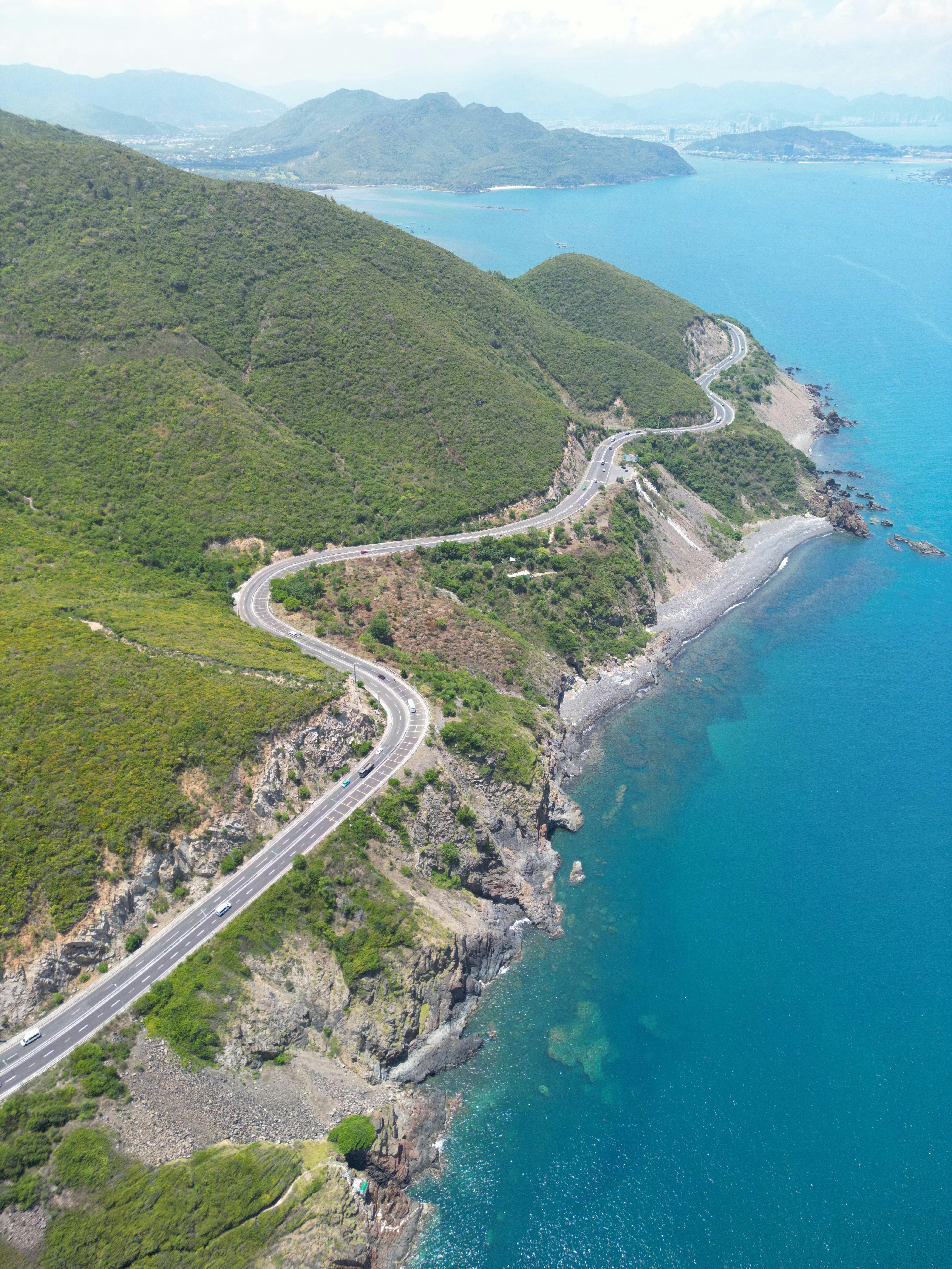 Gratis Una vista aerea di una pittoresca strada costiera che serpeggia tra lussureggianti colline in riva al mare in Vietnam, sotto un cielo limpido. Foto a disposizione