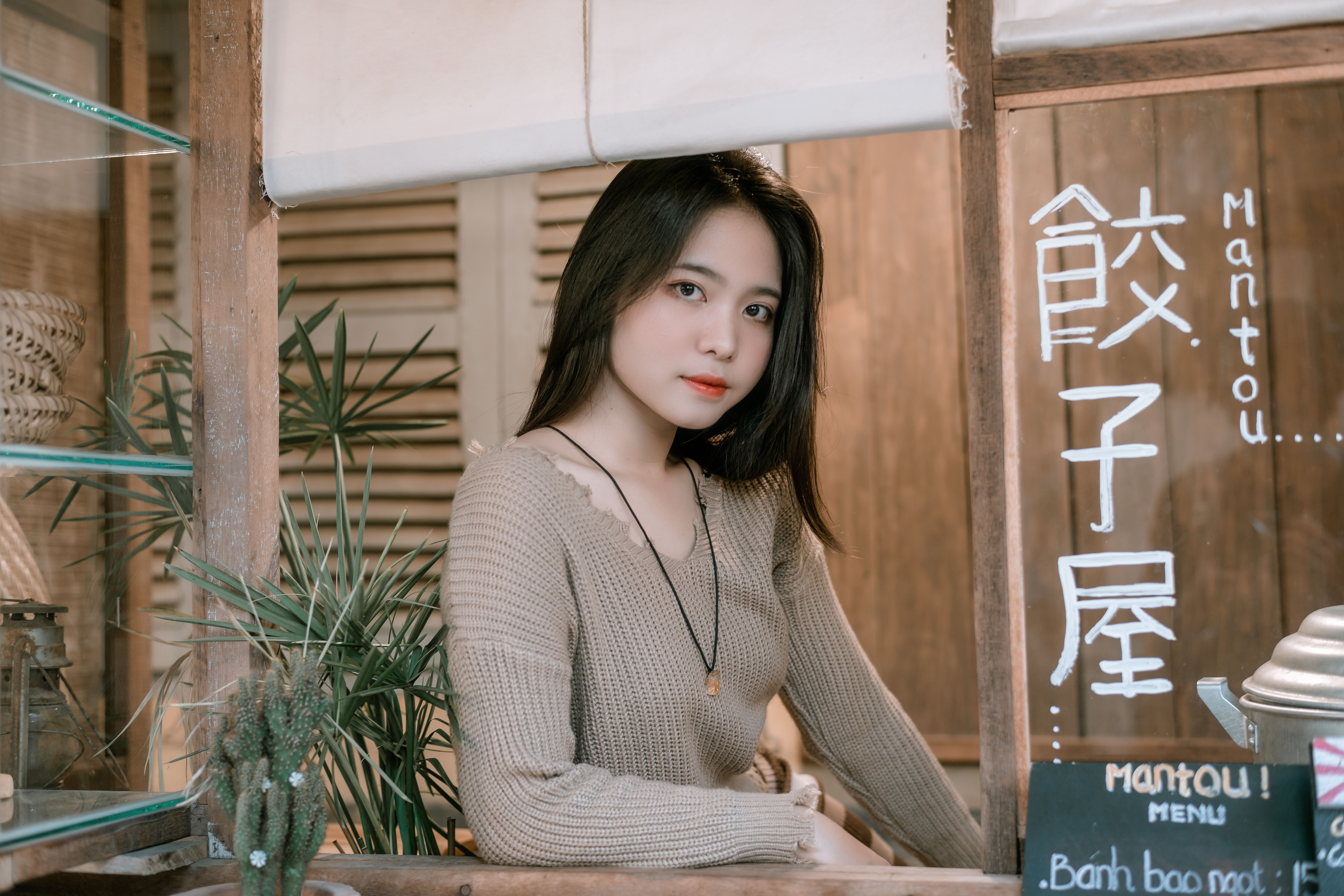 A young woman poses at a cozy cafe counter with a handwritten menu board in the foreground.
