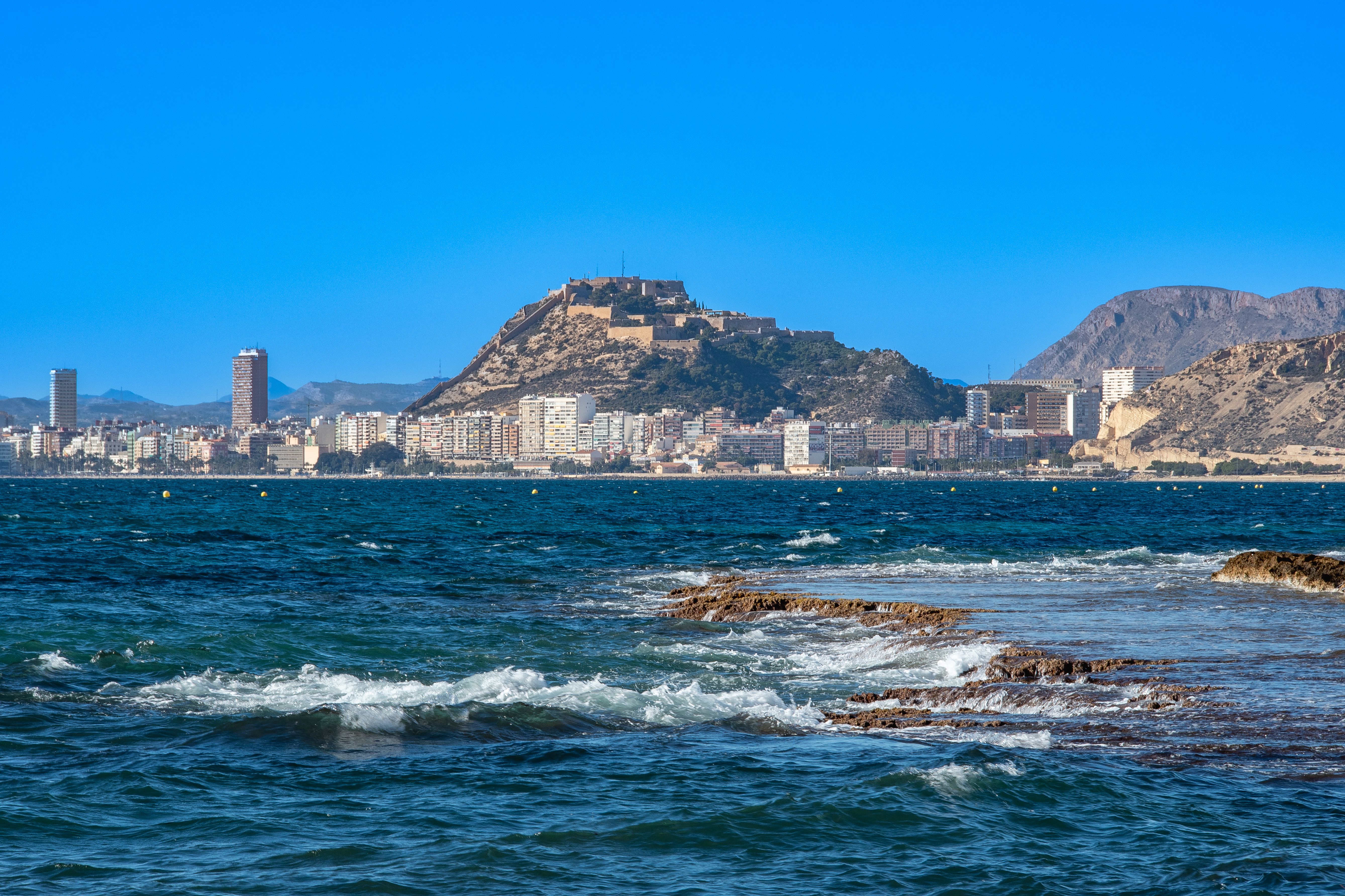 Vista costera de Alicante con el Castillo de Santa Bárbara al fondo y el mar Mediterráneo en primer plano
