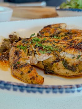 Juicy grilled chicken breast with fresh herbs served on a ceramic plate.