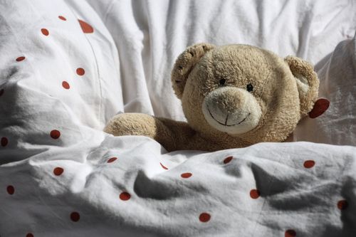 Free A plush teddy bear resting on a white comforter adorned with red polka dots, evoking warmth and comfort. Stock Photo