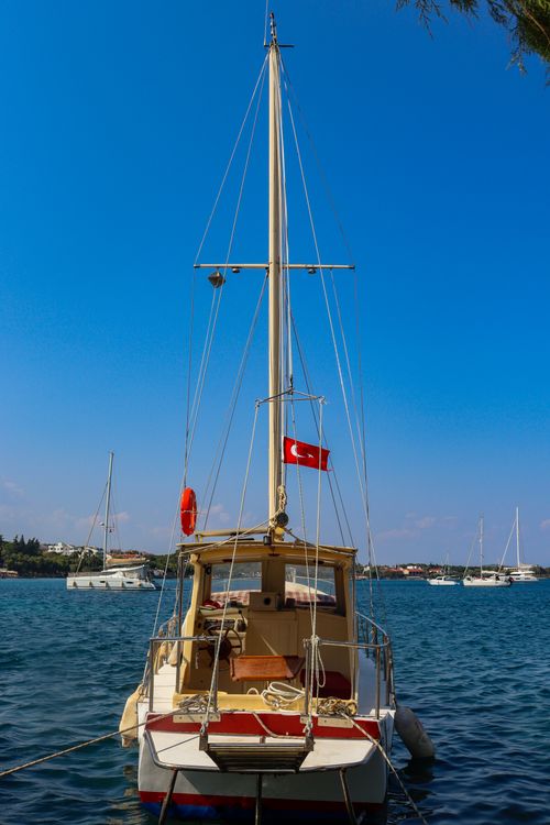 Free Sailboat displaying Turkish flag on calm waters under a clear blue sky. Stock Photo