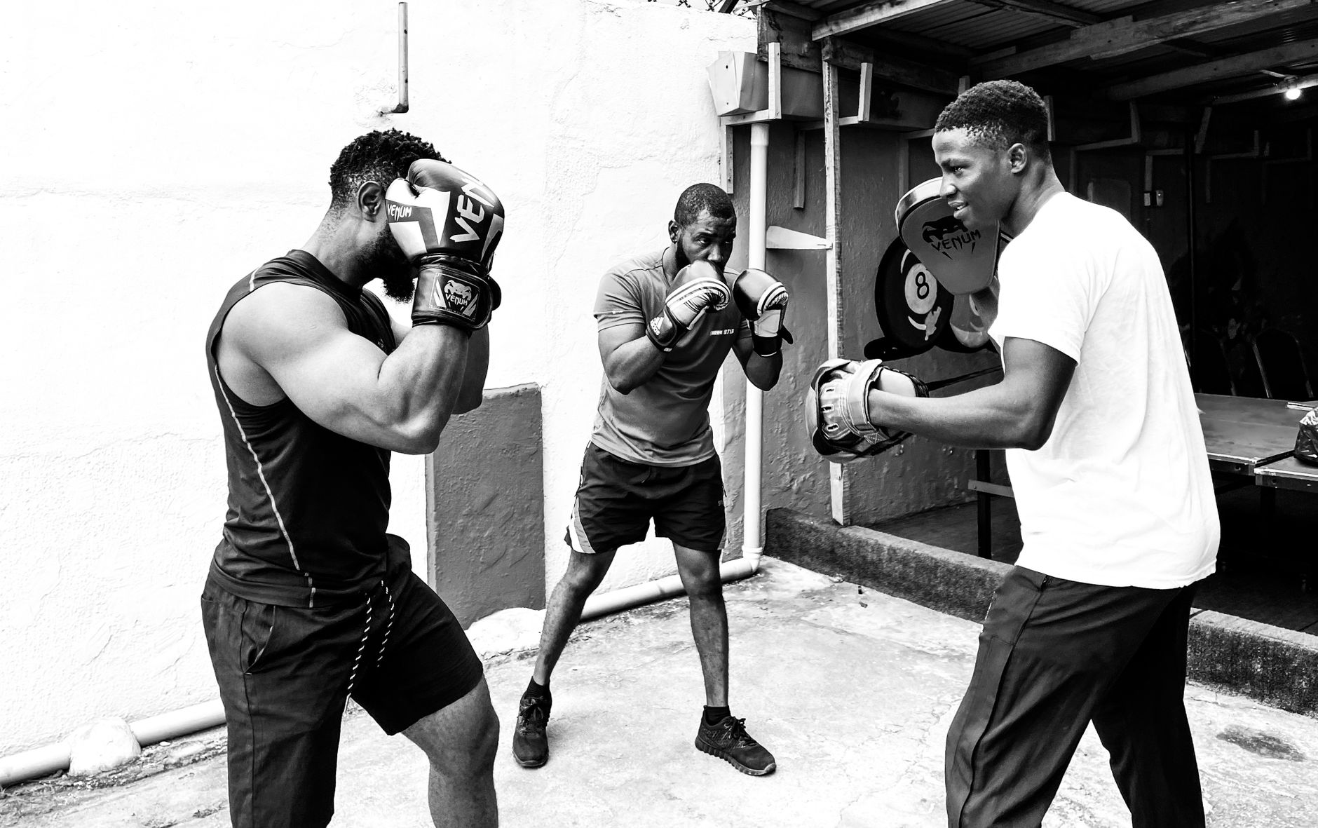 Three men engaged in a focused boxing training session with pads.