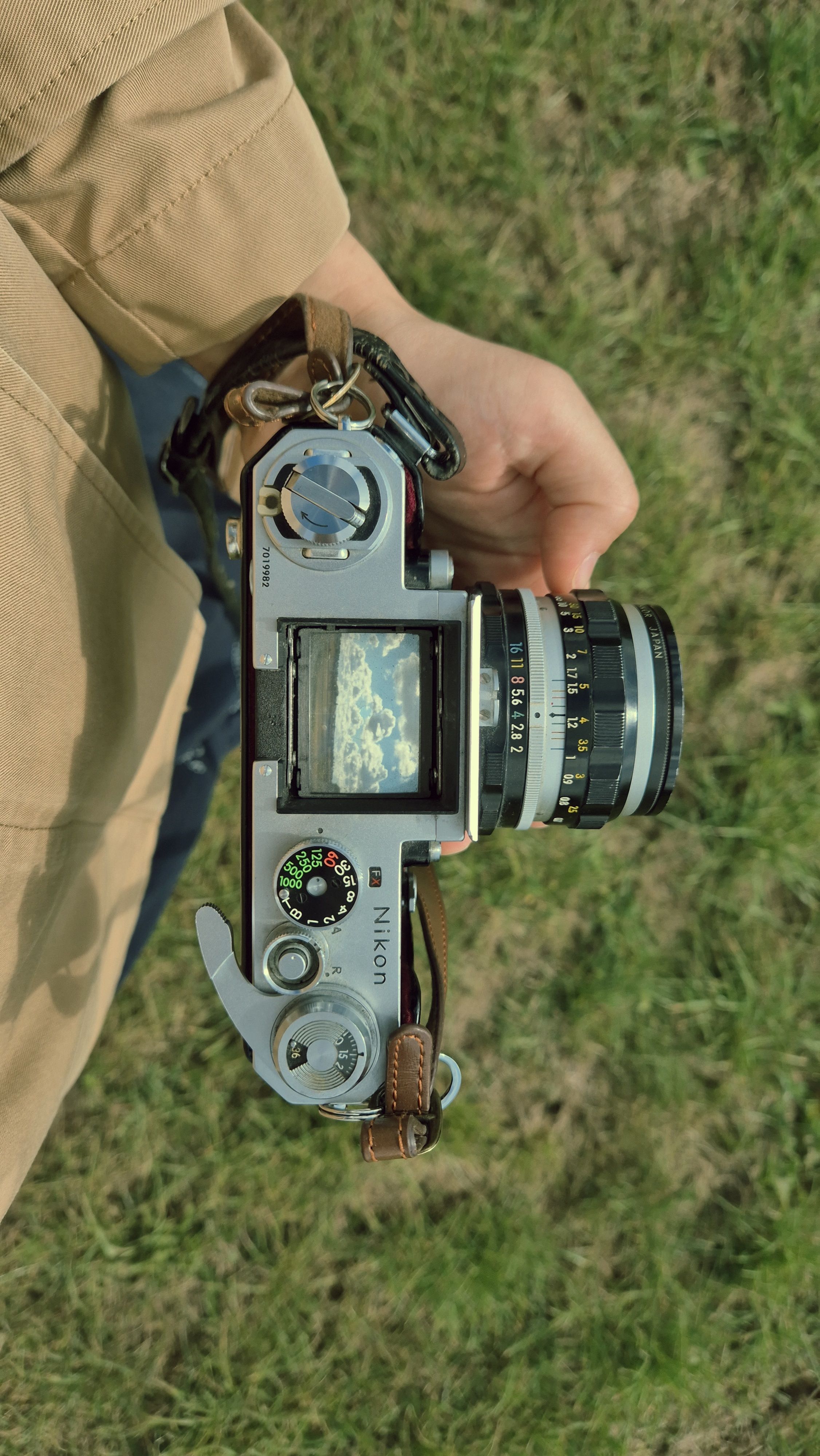 A photographer holds a vintage camera outdoors, capturing a scenic view.