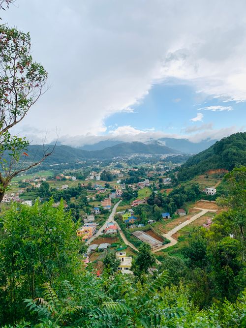 Free A picturesque view of a colorful mountain village surrounded by lush greenery and distant hills under a partly cloudy sky. Stock Photo
