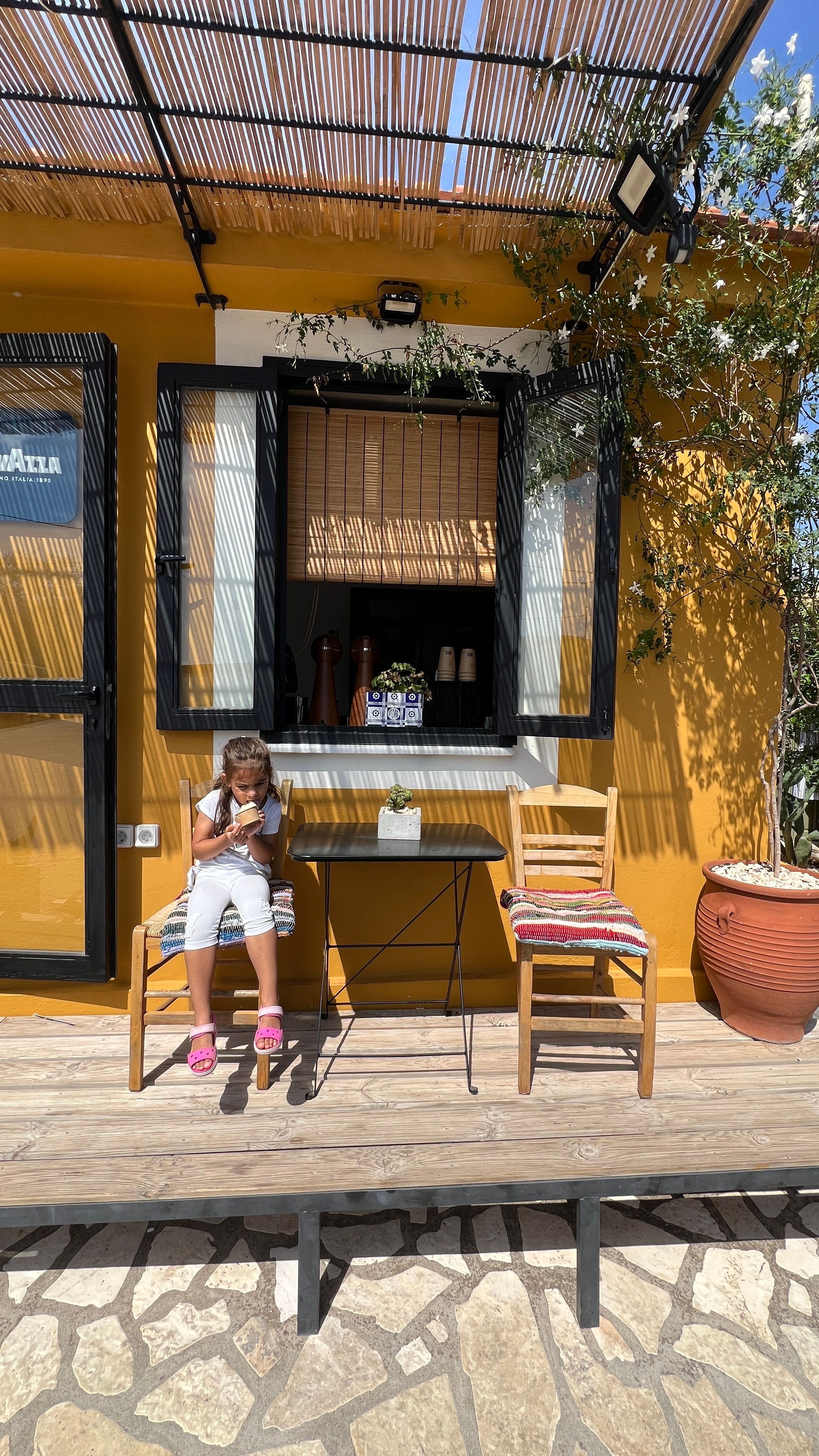 Fotomural Un café soleado con un niño leyendo afuera de una ventana encantadora.