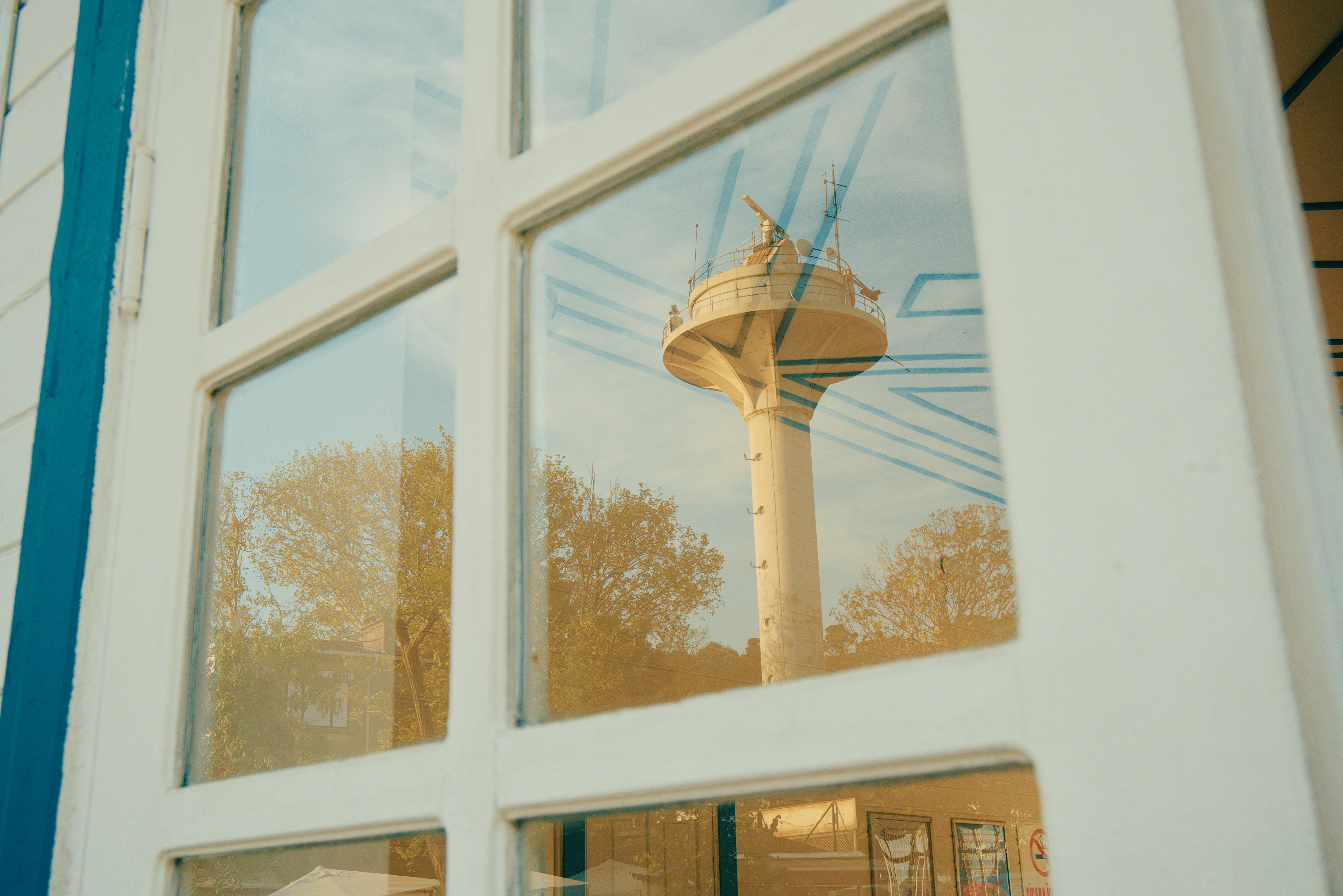 Kostenlos Faszinierende Spiegelung eines Turms durch ein Fenster mit Bäumen im Hintergrund. Stock-Foto