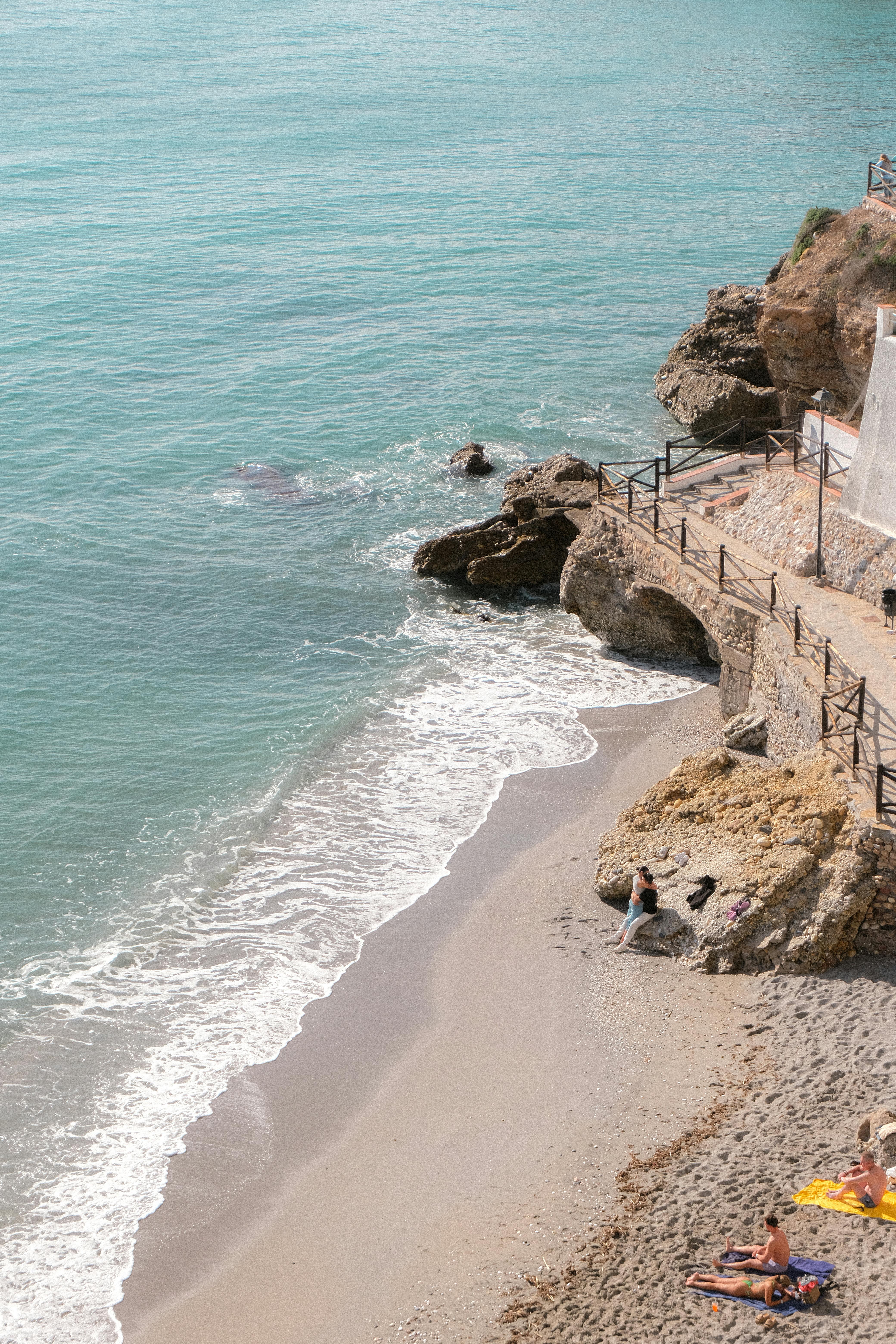 Aerial view of a serene beach in Nerja, Andalusia with turquoise water and sunbathers.