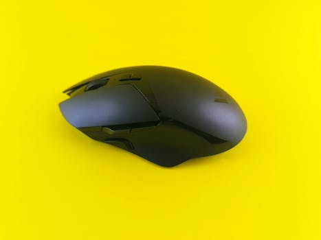 A modern black wireless mouse set against a vivid yellow backdrop.