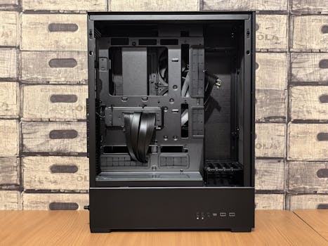 Black open computer chassis on table with wooden crate wallpaper.