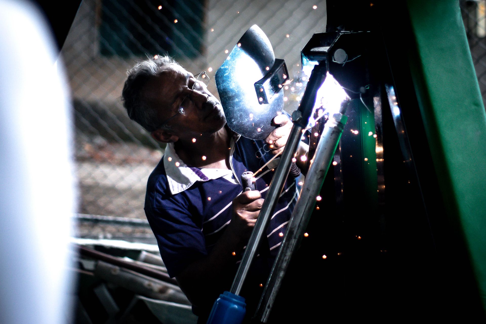 A professional welder working indoors, using safety equipment and producing bright sparks.