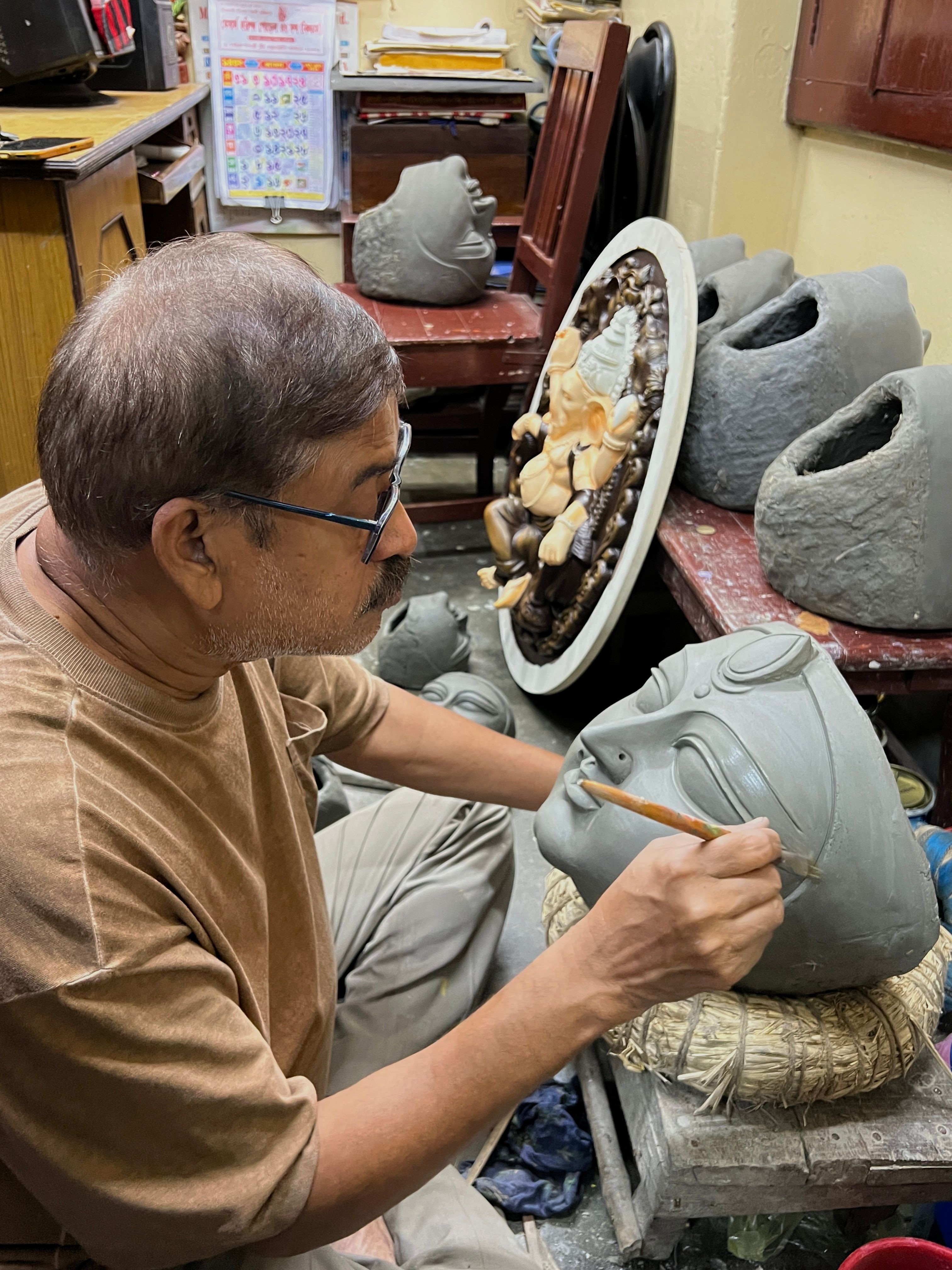 An artist passionately sculpts a traditional Hindu deity mask in a vibrant Kolkata workshop.