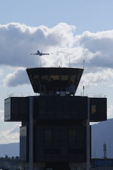 A passenger airplane takes off over the control tower at Geneva Airport, Switzerland, under a cloudy sky.
