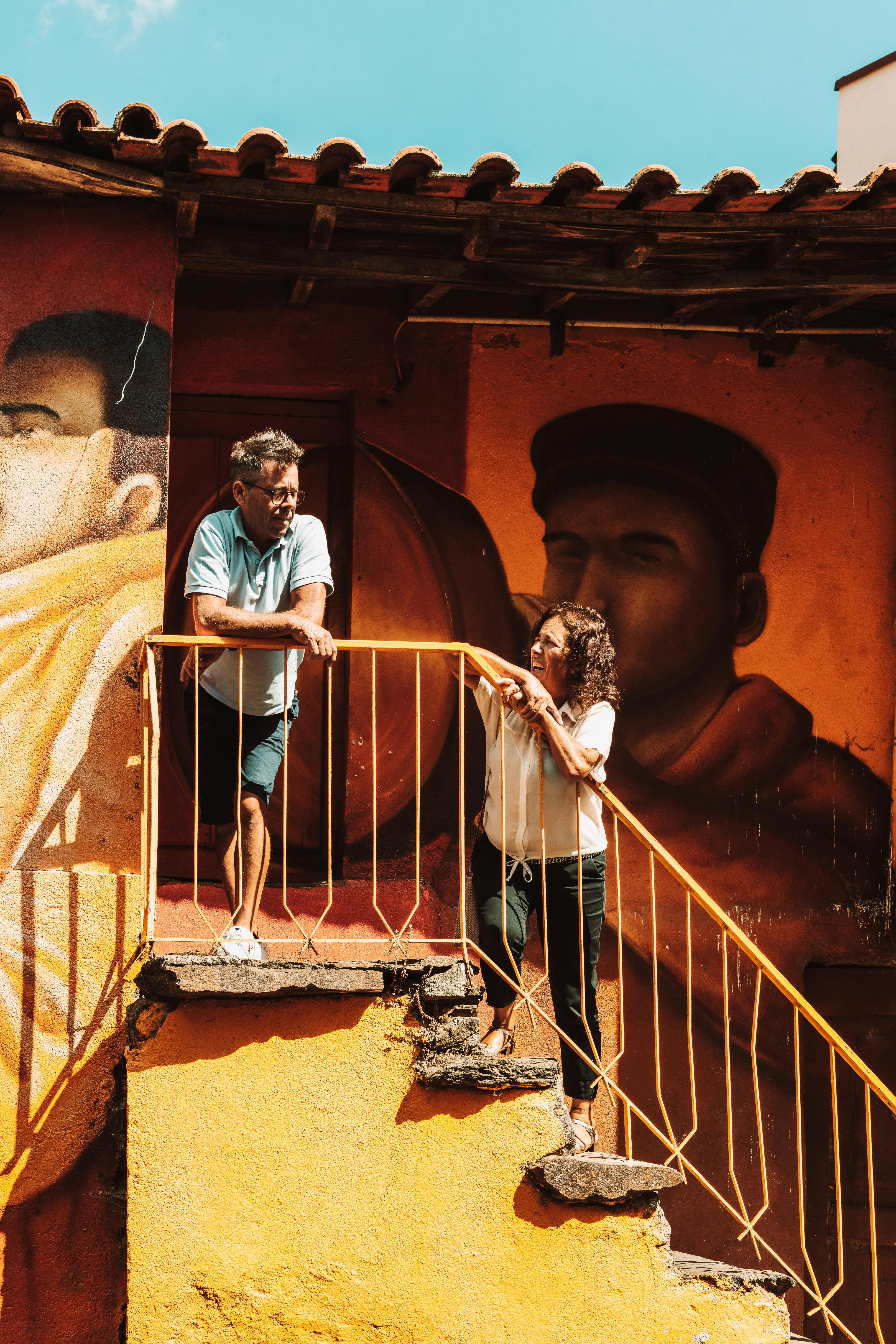 Two people engage on stairs in front of a vibrant mural in Macedo de Cavaleiros, Portugal.