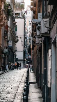 Discover the historic charm of a bustling narrow street in Naples, Italy, filled with life and architecture.