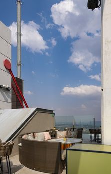 Cozy rooftop lounge area overlooking a modern city skyline under a bright blue sky.