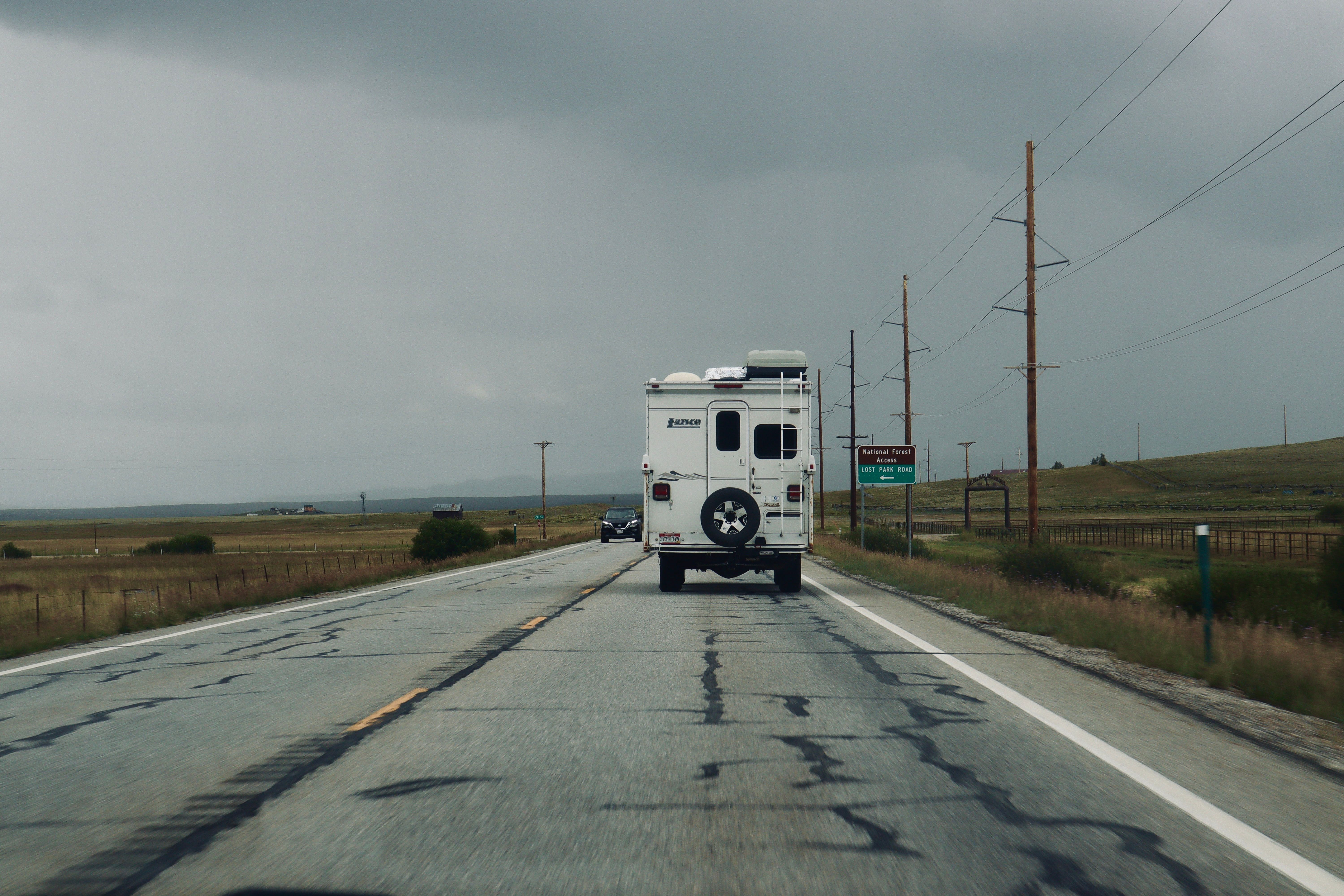 A lone RV travels down a deserted road under a cloudy sky, evoking adventure.