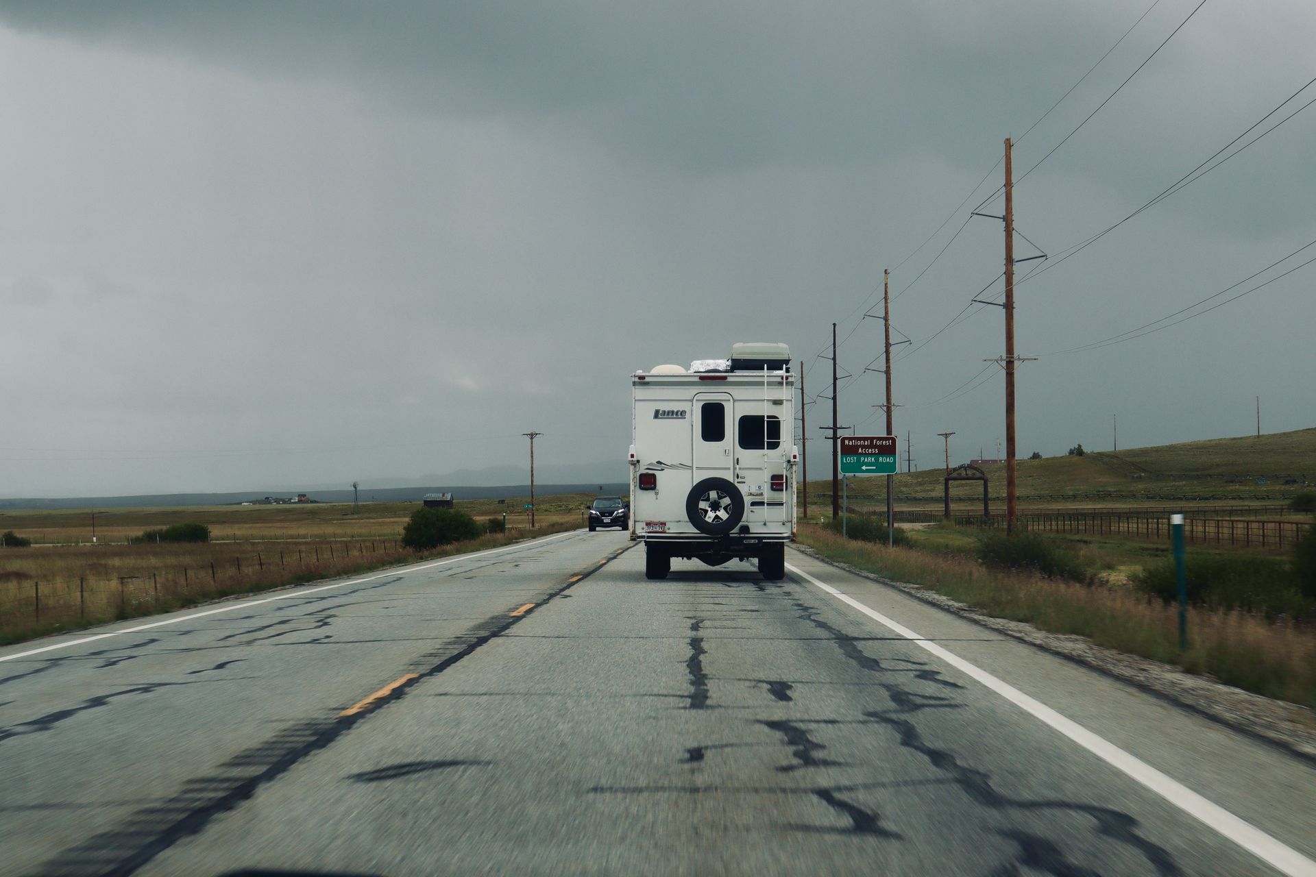 A lone RV travels down a deserted road under a cloudy sky, evoking adventure.