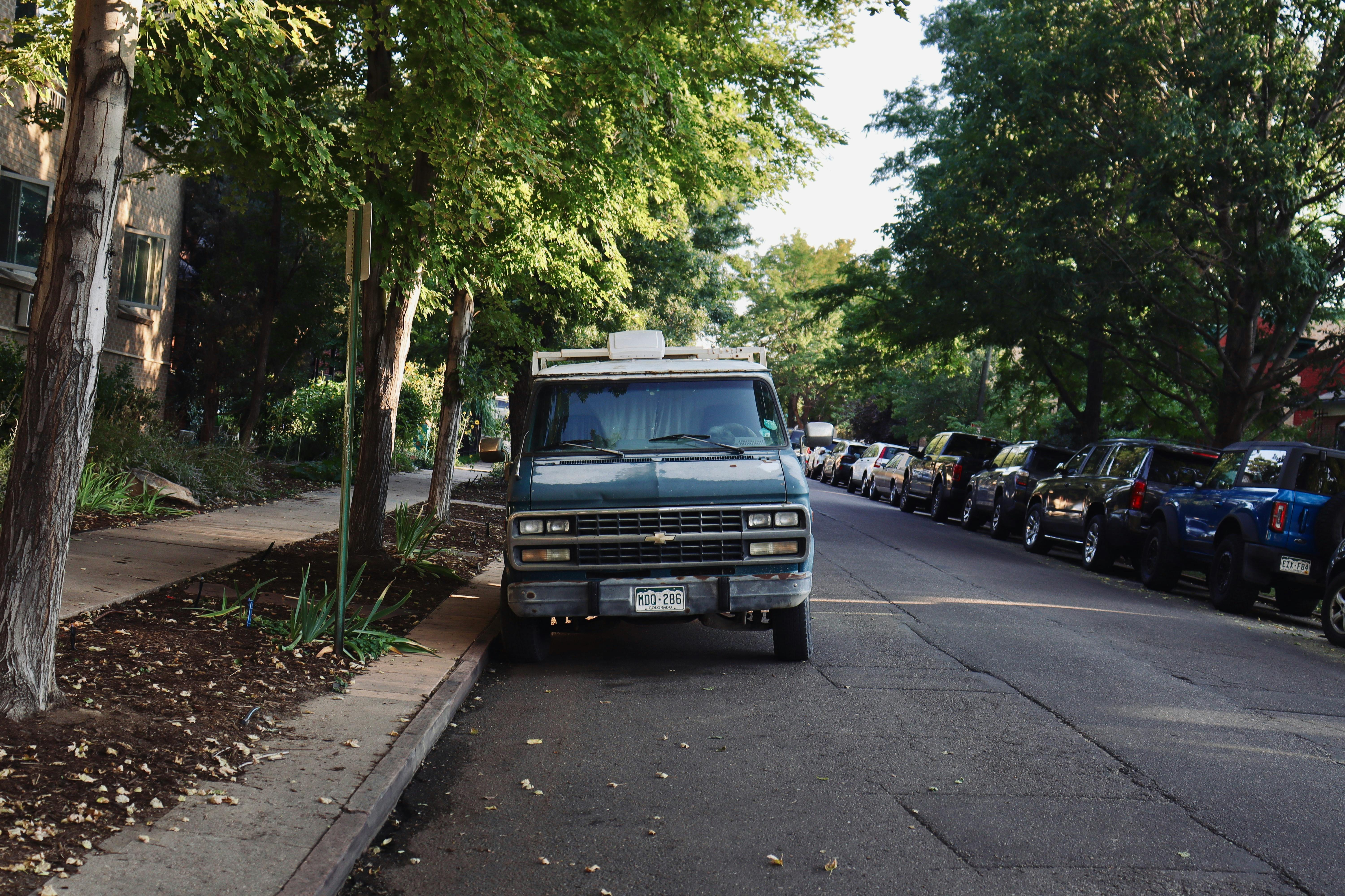 A classic van parked on a tree-lined street surrounded by residential buildings.