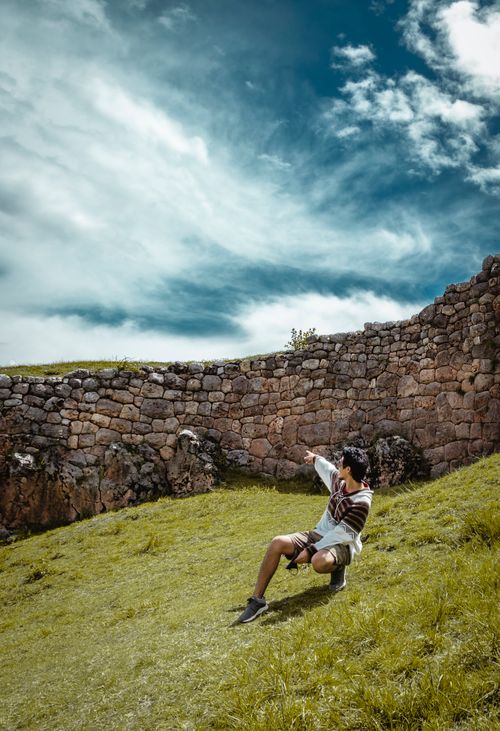 Free A person sitting leisurely by an ancient stone wall under a bright blue sky, showcasing historical travel adventures. Stock Photo