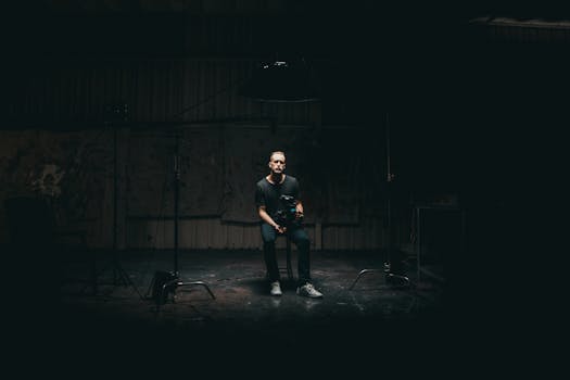 A cinematographer with camera gear sitting in a dimly lit studio setting.