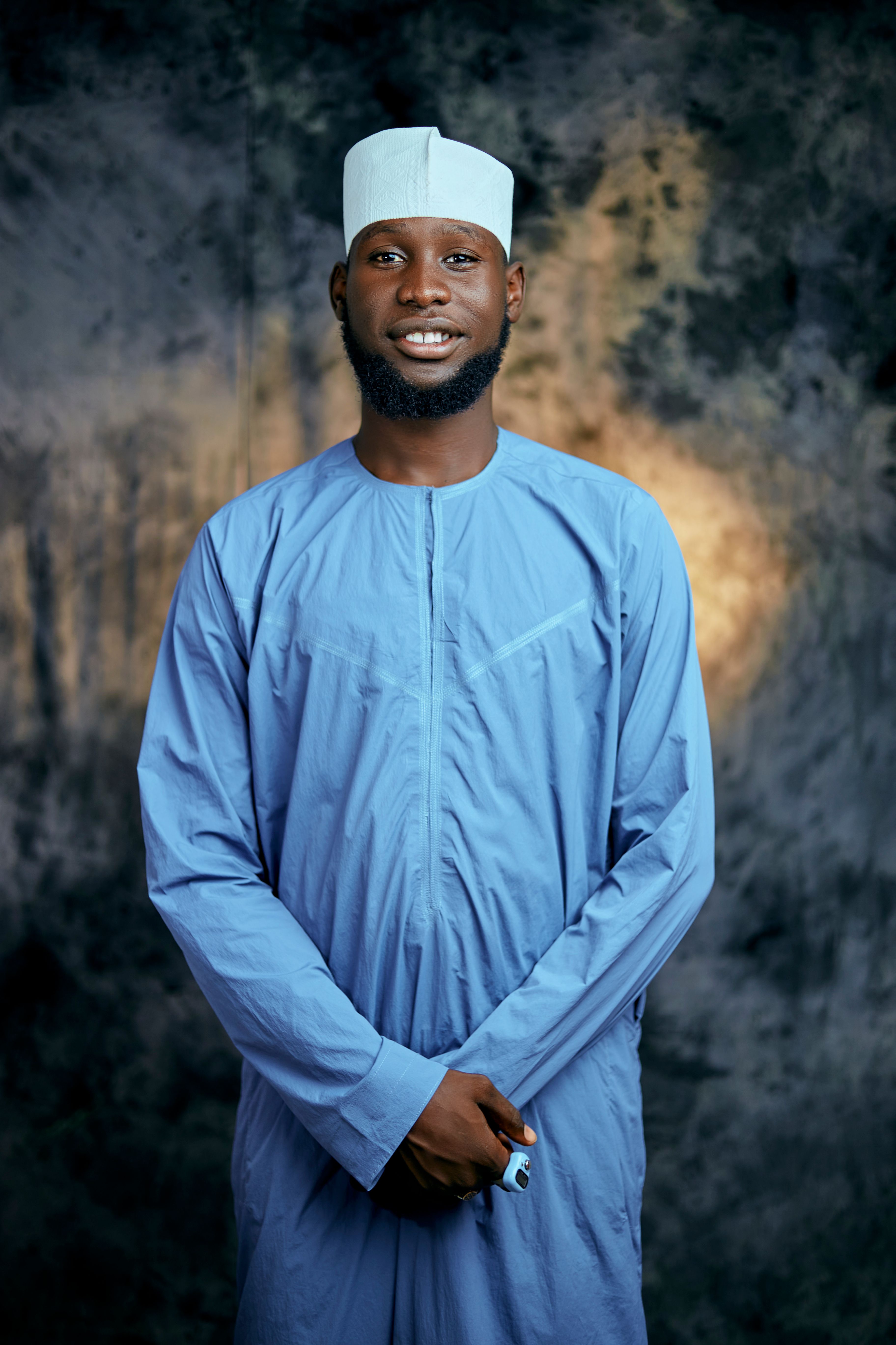 Professional portrait of a man in traditional blue attire against a neutral backdrop.