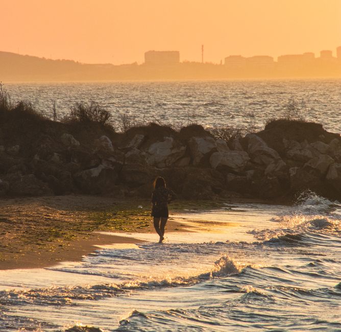Woman walking along the beach at sunset with ocean waves in a tranquil setting.