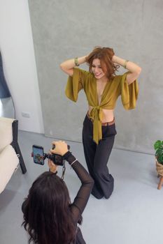 Photographer capturing a stylish woman posing in a contemporary studio environment.