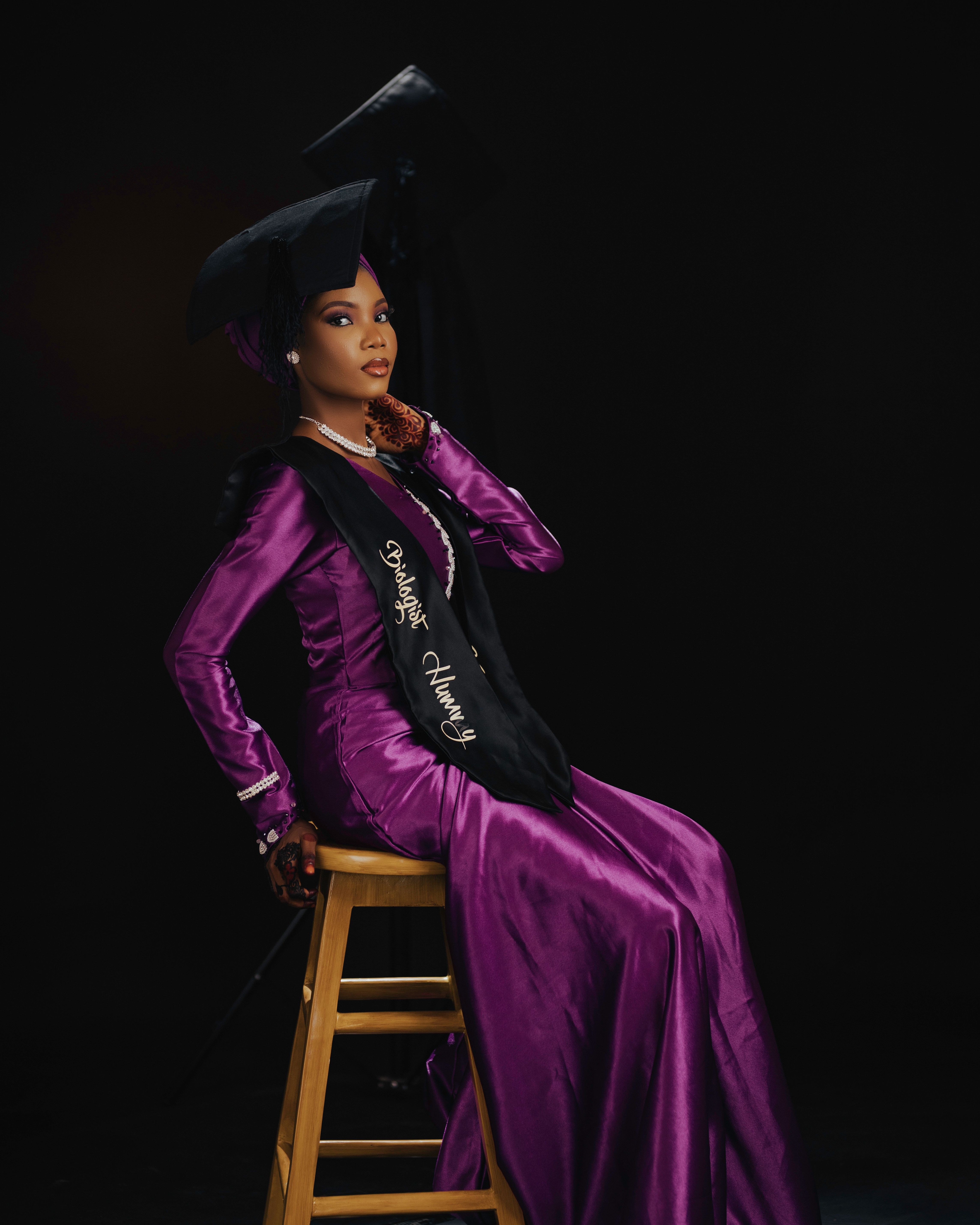 Portrait of a stylish female graduate in a vibrant purple gown against a dark background.