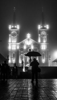 Moody night view of Baguio Cathedral in fog with silhouetted figures and umbrellas.