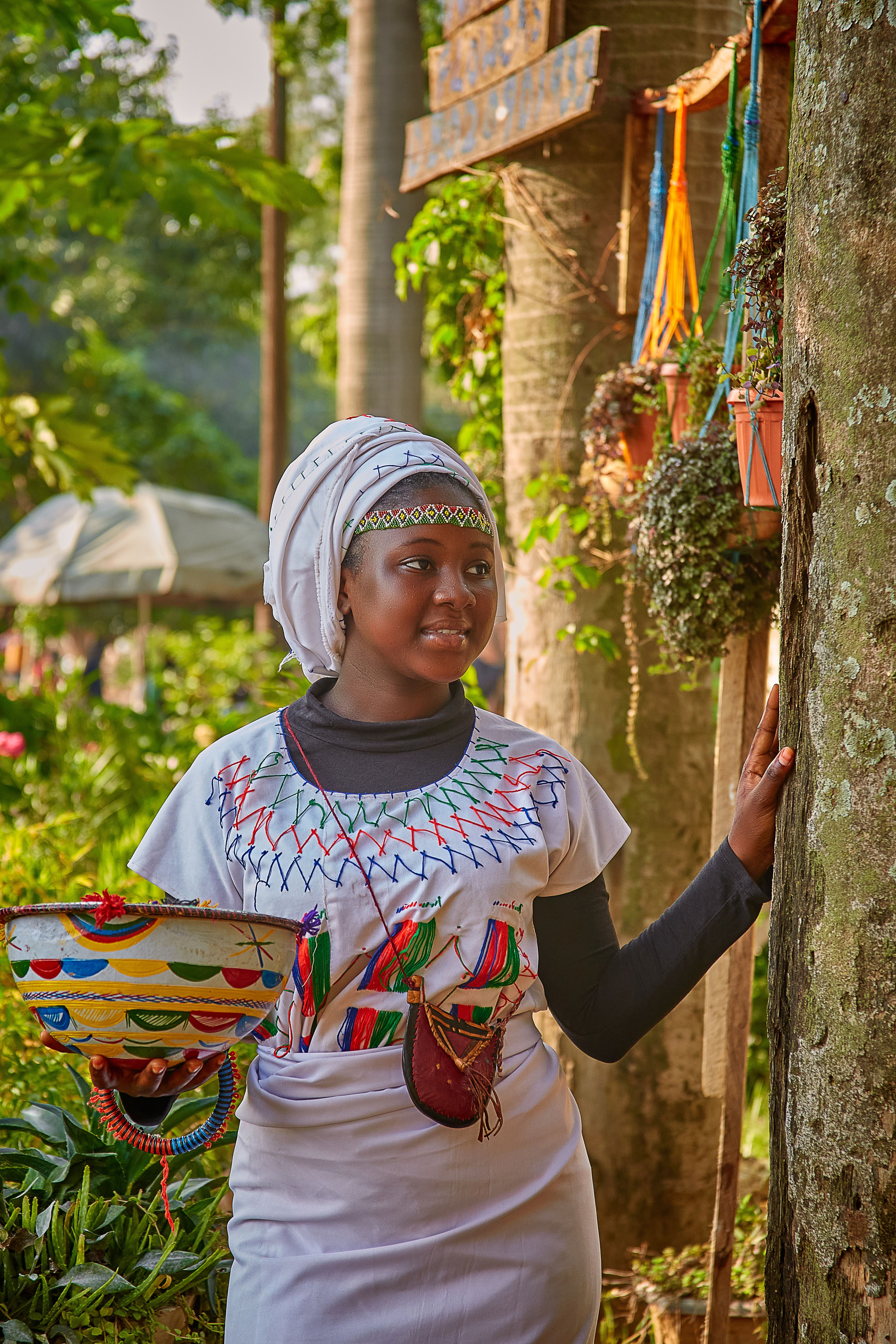 African woman in colorful traditional dress smiling outdoors, holding a basket.