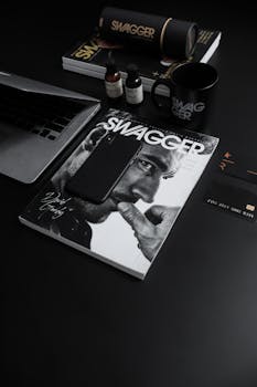 Stylish black desk layout with Swagger magazine, smartphone, and gadgets, showcasing modern lifestyle elegance.