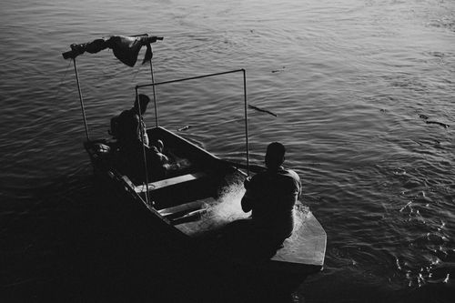 Free Two fishermen on a boat silhouetted against the sunset, casting nets into the water. Stock Photo