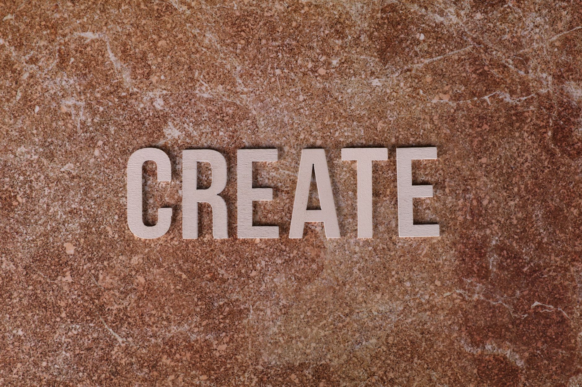 Inspiring CREATE text on a textured brown marble surface, promoting creativity.