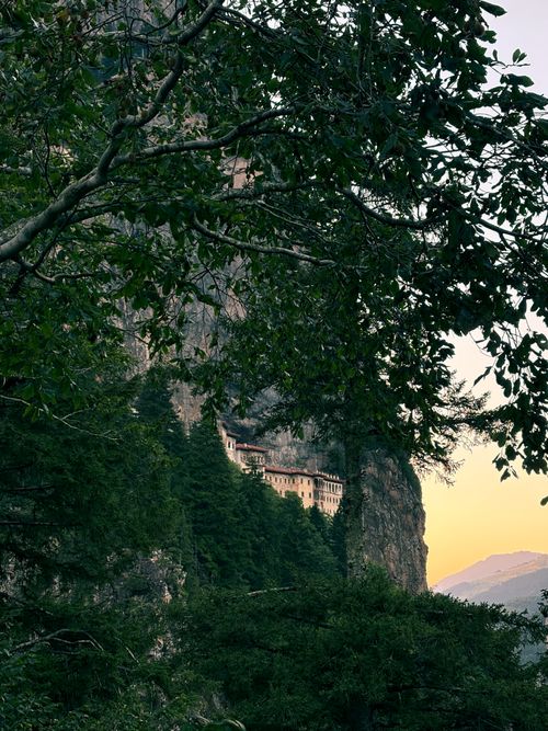 Free Sumela Monastery nestled in a lush, green mountain landscape at sunset. Stock Photo