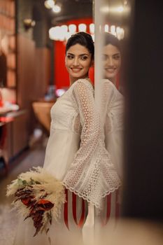Bride smiling in elegant boutique setting, holding a chic floral bouquet, reflecting on a mirror.