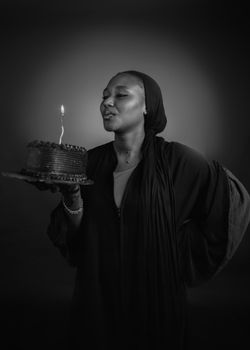 Black and white photo of a woman holding a cake with a lit candle, ready to make a wish.