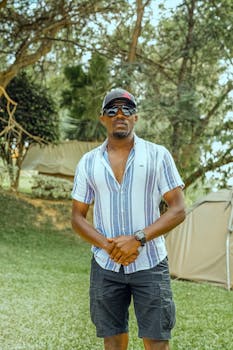 Casually dressed man standing outdoors next to a tent, relaxed summer vibe.