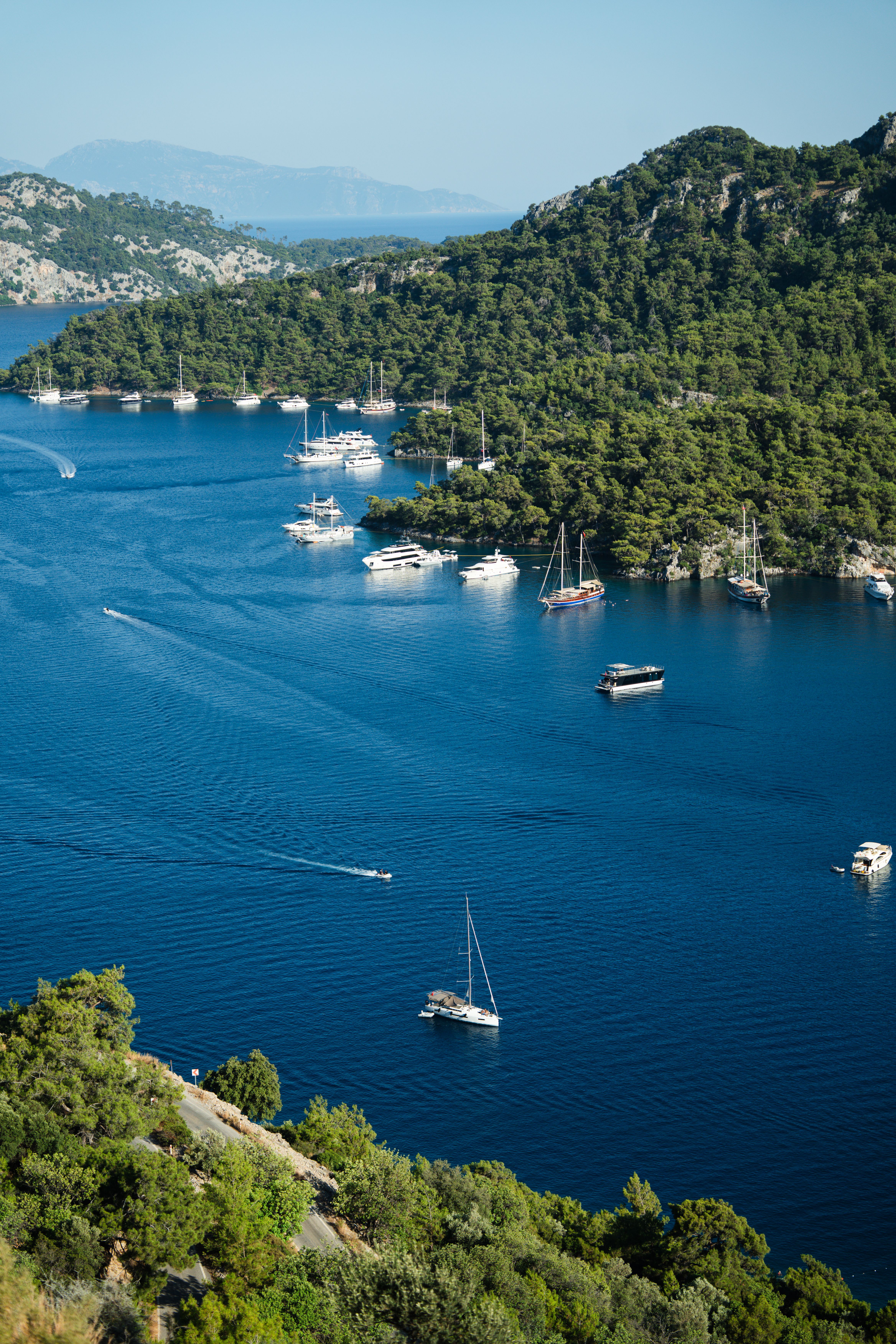 A scenic aerial view of boats anchored in a tranquil blue bay surrounded by lush hills.