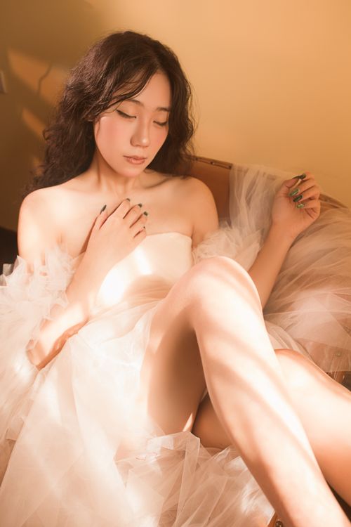 Free A serene moment of an elegant woman in a soft dress warmly lit by sunlight. Stock Photo