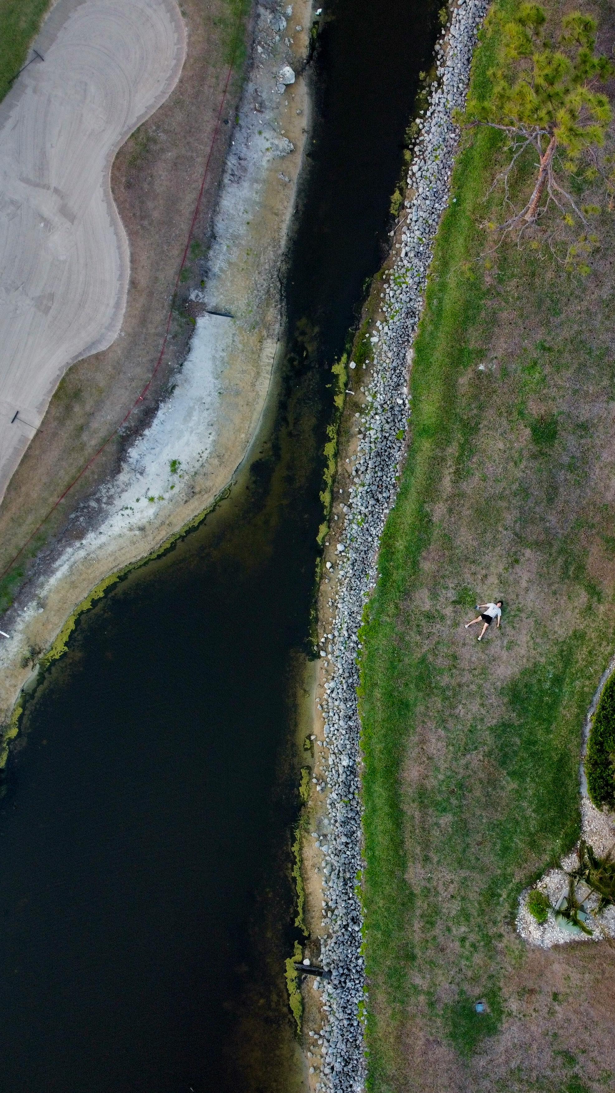 Kostenlos Luftaufnahme einer Person, die im Gras neben einem Flussufer in Fort Myers, Florida, liegt. Stock-Foto