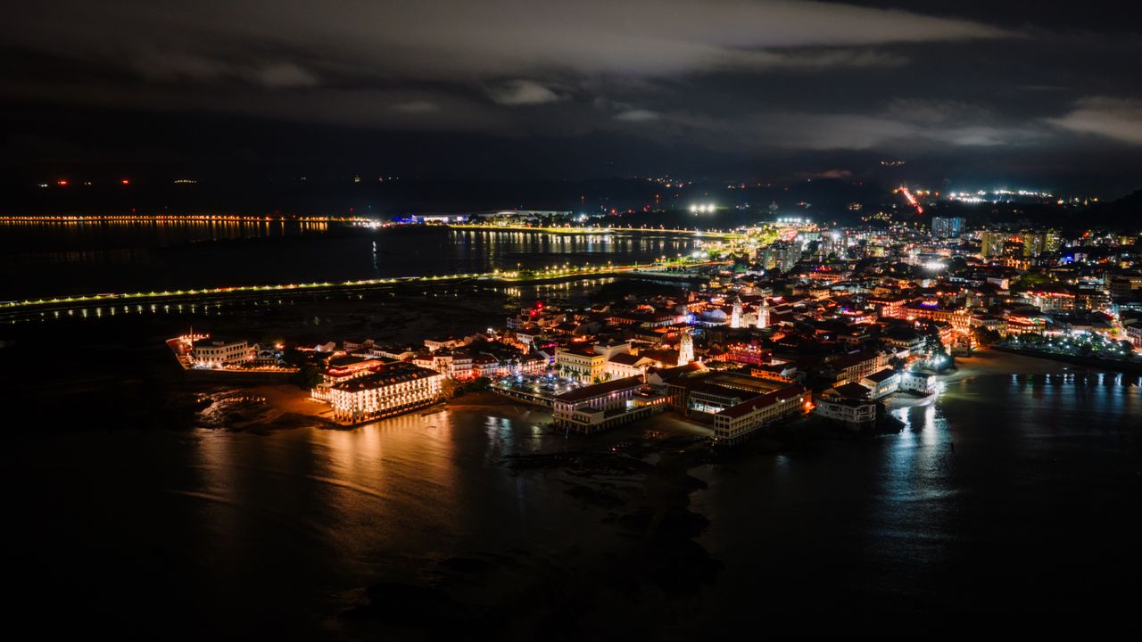 Aerial night view of an illuminated historic waterfront district with a lit church tower