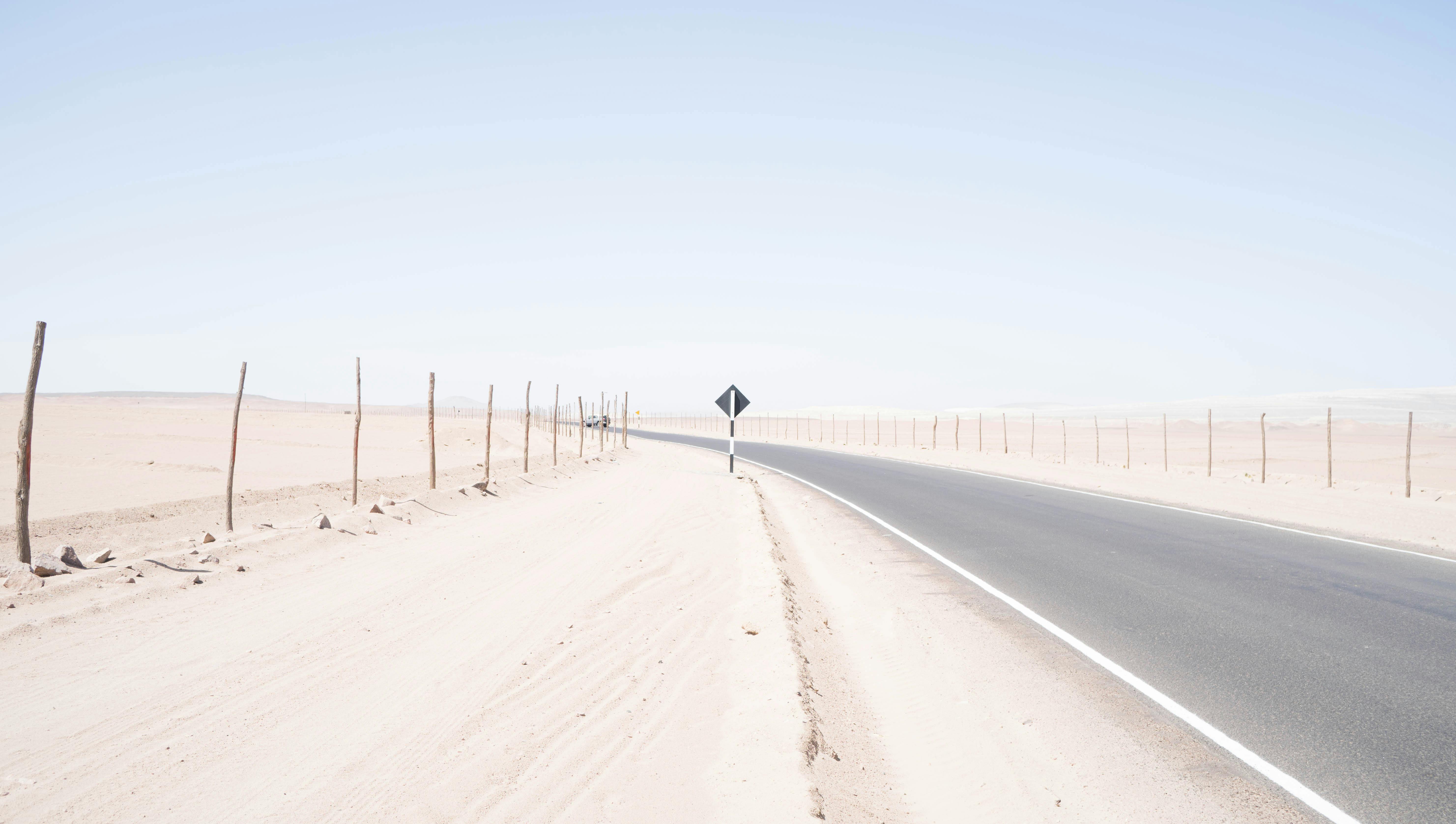 一条荒无人烟的道路蜿蜒穿过广阔干旱的沙漠，在明亮的蓝天下，捕捉到了孤独与旅行的本质