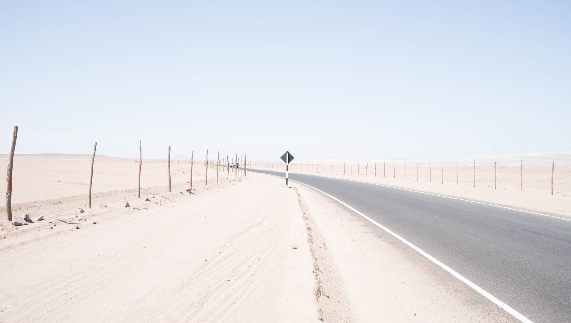 A deserted road winds through a vast, arid desert under a bright blue sky, capturing the essence of solitude and travel.