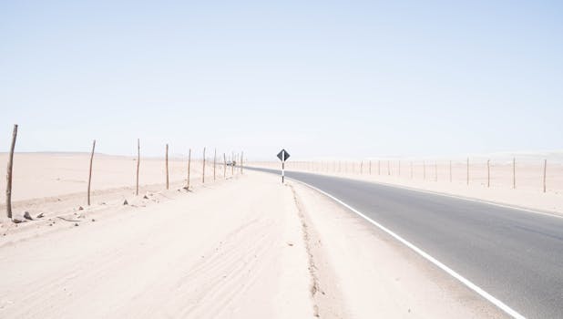 一条荒无人烟的道路蜿蜒穿过广阔干旱的沙漠，在明亮的蓝天下，捕捉到了孤独与旅行的本质