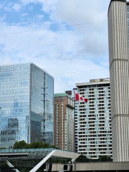 Modern skyscrapers in downtown Toronto featuring a Canadian flag under a blue sky.