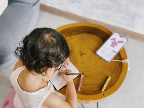 Free Young child drawing at a table with a smartphone displaying cartoon nearby, shot indoors. Stock Photo